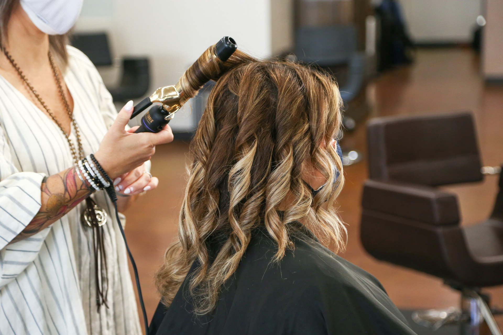woman in stripped shirt curling a customer's hair
